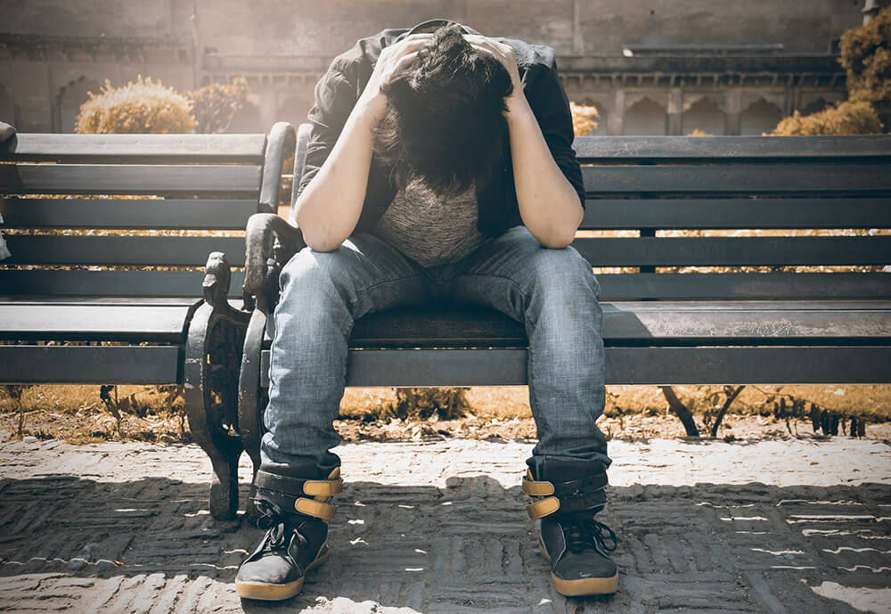 Man sitting on bench with head in hands